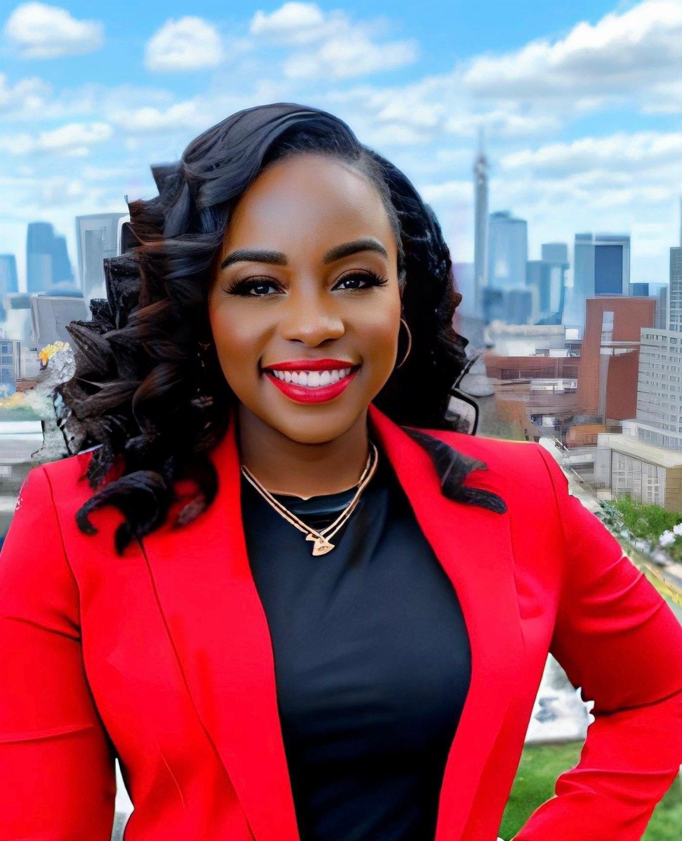 Woman in red blazer smiling with a cityscape background under a partly cloudy sky.