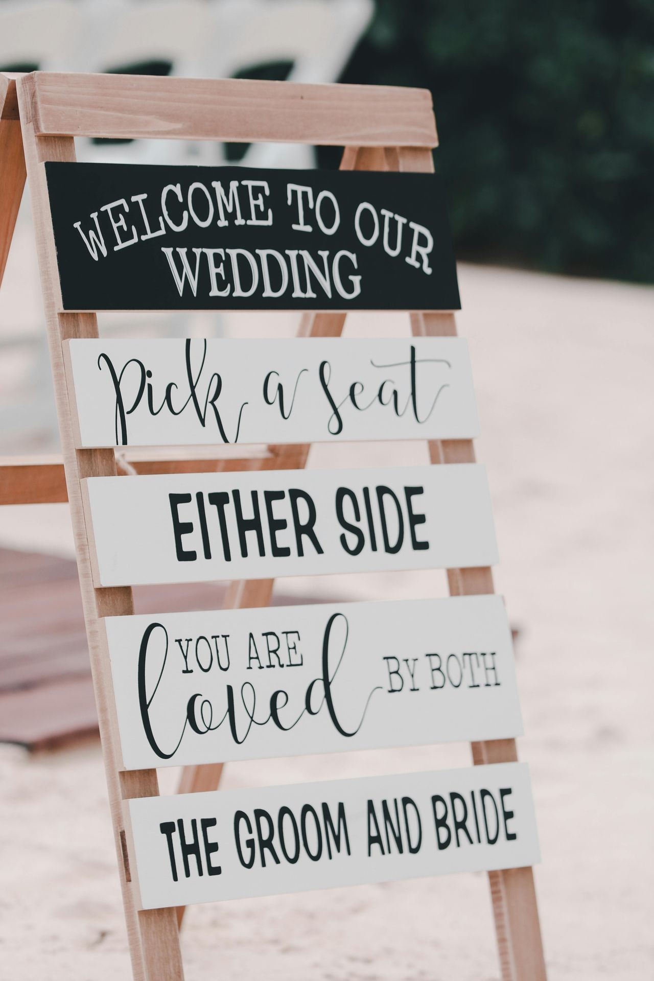 Wedding sign with messages welcoming guests and seating choices on sandy beach background.